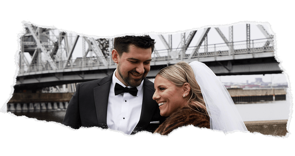 Newlyweds smiling by a historic Duluth aerial lift bridge in winter.