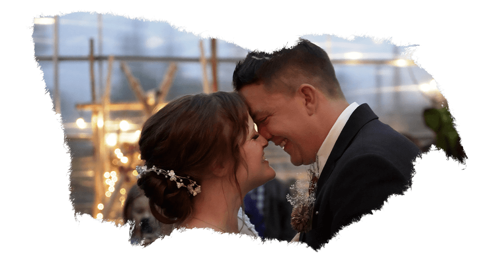 Newlyweds kissing under twinkling lights at an evening reception.