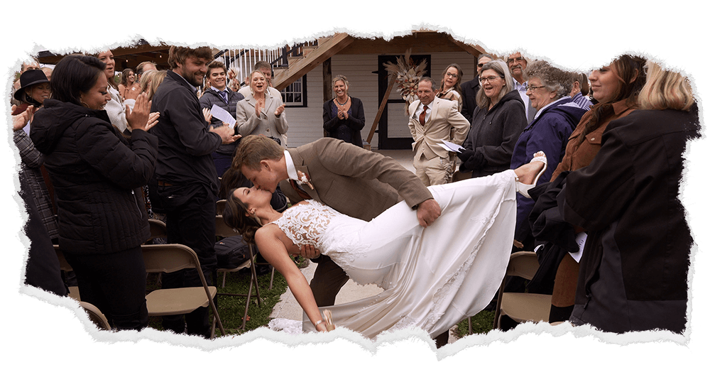 Newlyweds sharing a playful dip kiss at their outdoor wedding celebration in Duluth, with guests applauding.